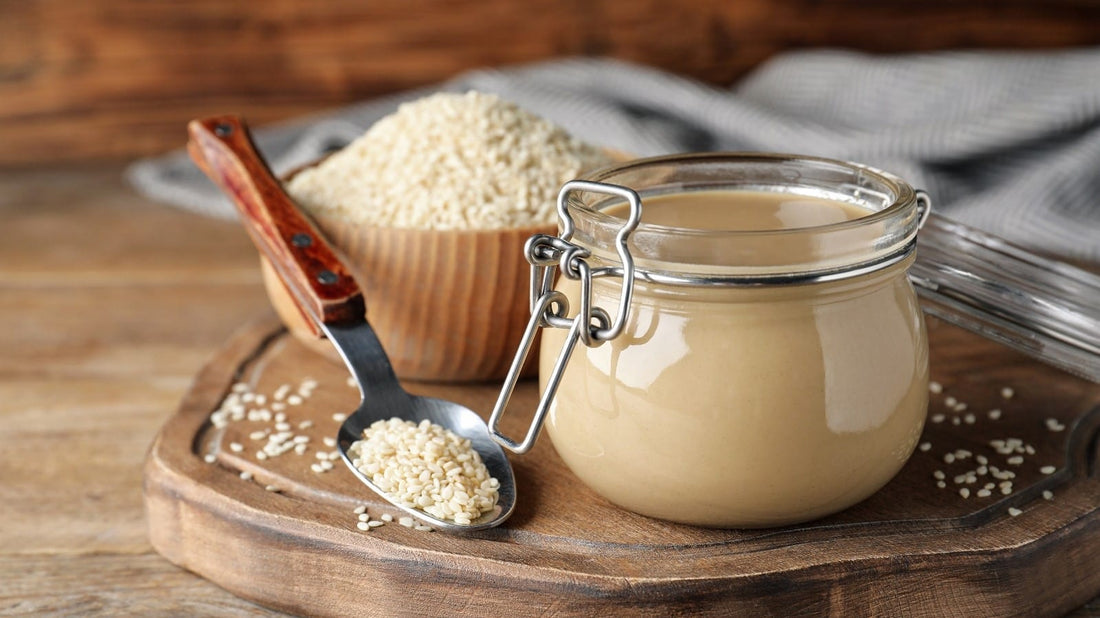 FUN Sesames Tahini Paste | A jar of tahini sauce, a bowl of sesame seeds, and a spoon rest atop the cupboard, ready for culinary adventures.