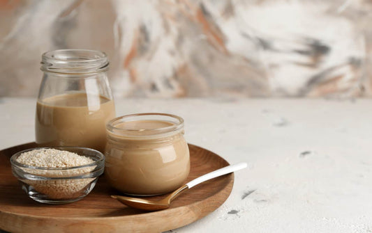 FUN Sesames Tahini Spread | Two jars of tahini stand beside a bowl of sesame seeds, inviting exploration with a wooden spoon.