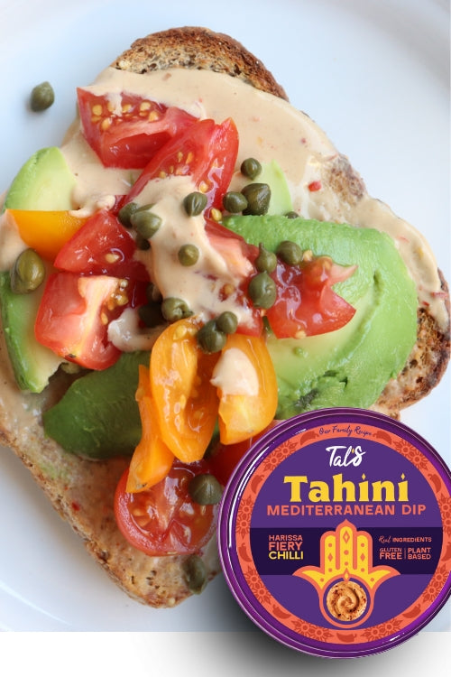 The image is a close-up food photograph featuring an open-faced toast topped with fresh vegetables and creamy tahini dip, with a jar of Tal’s Tahini Mediterranean Dip prominently placed in the lower-right corner.