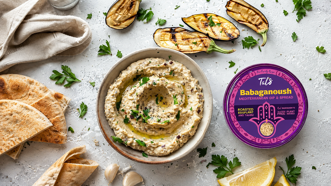 A bowl of creamy babaganoush garnished with parsley and olive oil, surrounded by pita bread, grilled eggplant, lemon, and a Tal’s Babaganoush container on a light stone surface.