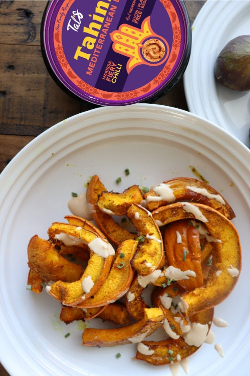 Roasted Pumpkin with Cumin on a plate featuring Tal's Tahini Mediterranean Dip in Harissa Fiery Chili flavor.