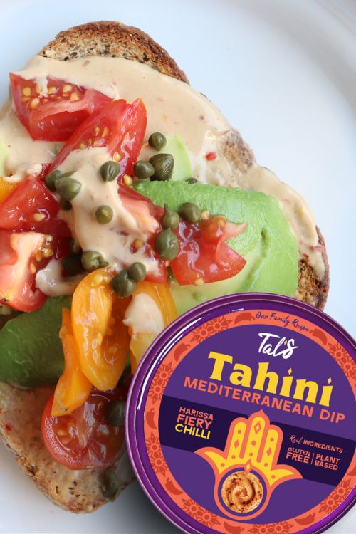 A sandwich on a plate with Tal's Mediterranean Harissa Fiery Chili Tahini Dip featured at the bottom right.